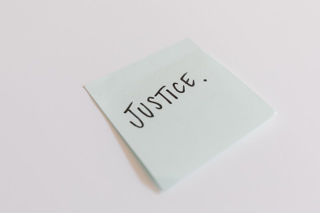 A close-up shot of a sticky note with the word 'Justice' handwritten on it.
